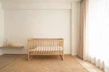A Japandi nursery with a light oak crib, linen curtains and a woven jute rug